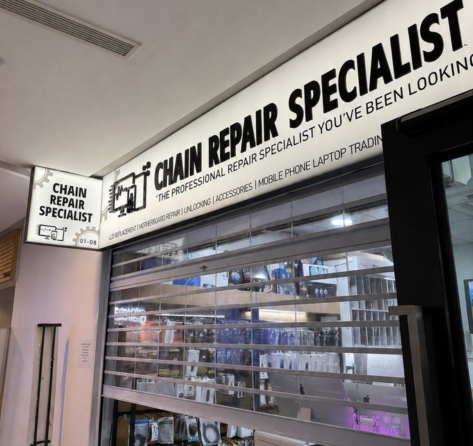 A storefront sign reads 'CHAIN REPAIR SPECIALIST' with the tagline 'THE PROFESSIONAL REPAIR SPECIALIST YOU'VE BEEN LOOKING FOR,' advertising services like laptop repair, mobile phone, and unlocking.