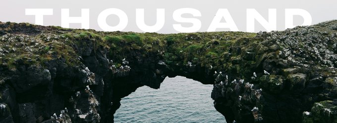 A dramatic coastal landscape features a natural stone arch over turquoise waters, with seabirds perched along the rocky cliffs, while the word "THOUSAND" appears in bold white text across the top, likely referencing the NFT collection's theme of appreciating art for its intrinsic value rather than financial gains.