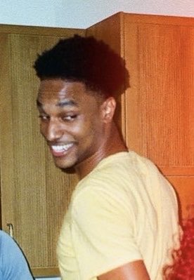 A young man with short curly hair smiles warmly while wearing a yellow t-shirt, standing in a kitchen with wooden cabinets. The image appears to serve as the subject or inspiration for a creative artwork featuring $ANSEM, referenced alongside the "Black Bull" themed sketch mentioned in the post.