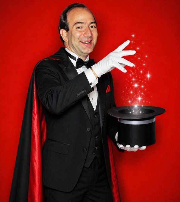 A smiling magician in a black tuxedo with a red-lined cape and white gloves performs magic, pulling sparkling stars from a black top hat against a red background.