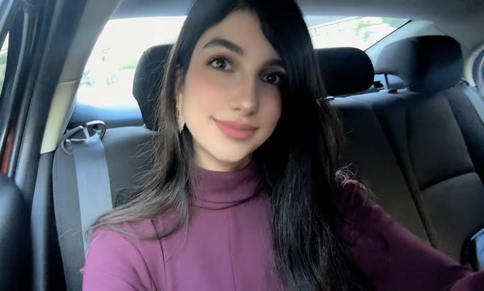 A selfie of a young woman with long dark hair wearing a plum-colored turtleneck, sitting in the passenger seat of a car.