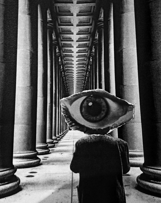 A surreal black and white composite image showing a figure in dark clothing with a giant realistic eye in place of a head, standing in a corridor lined with tall columns.