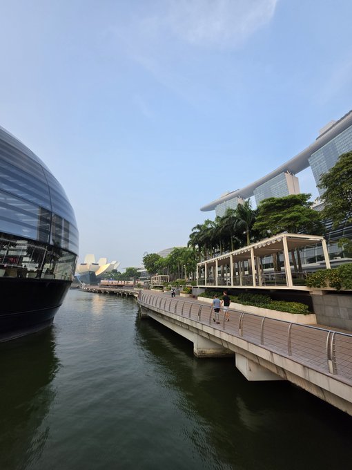A scenic daytime view of Marina Bay Sands in Singapore, showing the waterway, a pedestrian bridge, and the distinctive lotus-shaped ArtScience Museum.