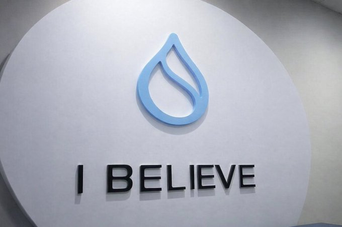 The image features a large white sign with a blue logo that reads "I Believe". The sign is displayed prominently against a gray wall, making it stand out as an advertisement or message for the brand. The text "Believe Sui" suggests that the company's name might be related to water or hydration in some way. However, there are no other texts or details about the product or service associated with this logo.