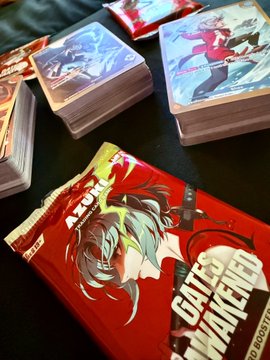 The image features a collection of anime trading cards, specifically the "Gates Awakened" series, neatly arranged on a table or countertop. The cards are displayed in various positions, showcasing their vibrant colors and intricate artwork. The packaging for these cards is also visible, adding to the overall presentation. The post about the anime trading cards seems to be promoting the release of new releases from the "Gates Awakened" series, highlighting the excitement surrounding this particular collection.