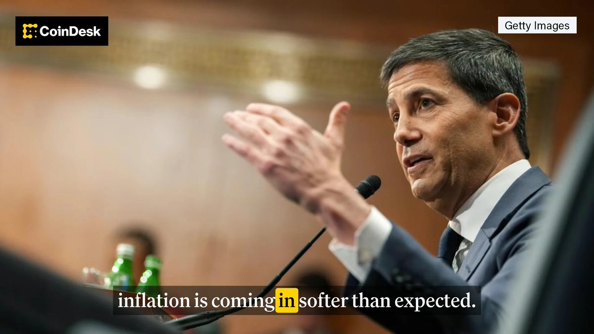 A man in a suit gestures while speaking at a formal hearing, with the CoinDesk logo in the corner and a caption reading "inflation is coming in softer than expected," referencing the U.S. Federal Reserve's positive economic outlook mentioned in the post.