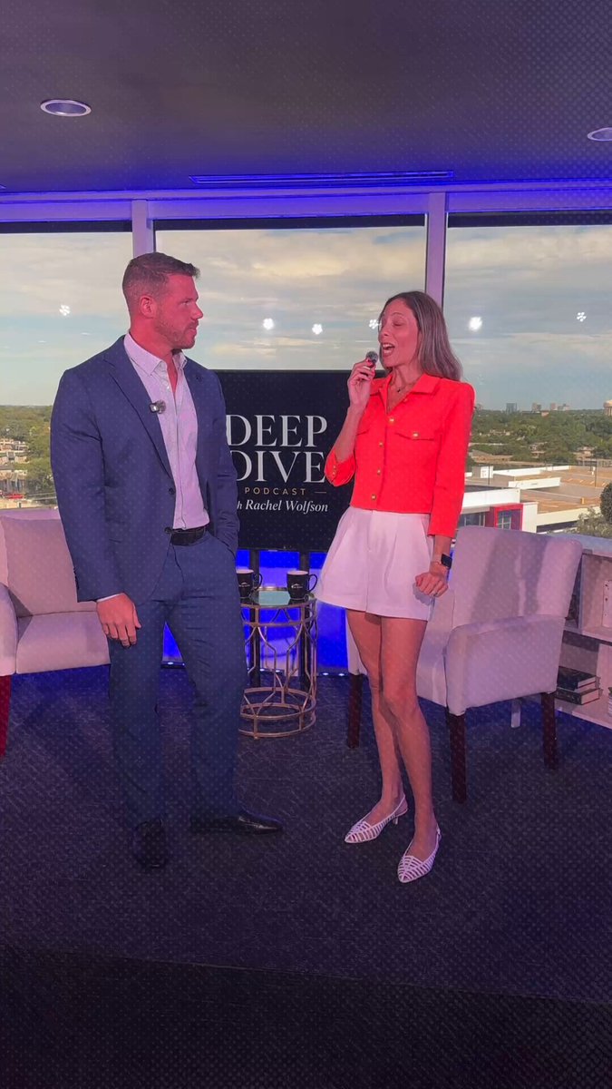 The image shows a man wearing a suit and tie standing next to a woman who is dressed in a red shirt and white skirt. They are both holding microphones, suggesting that they might be hosting or participating in an event related to cryptocurrency or digital assets. The background features a TV screen displaying the words "Deep Dive" and "XRP ETF", indicating that this could be part of a podcast discussion about XRP or other digital assets.