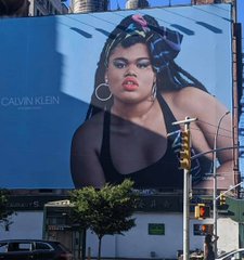 A large billboard advertisement features a plus-size model wearing a black bra and a colorful headscarf, with 'CALVIN KLEIN' branding visible on the left side of the image.