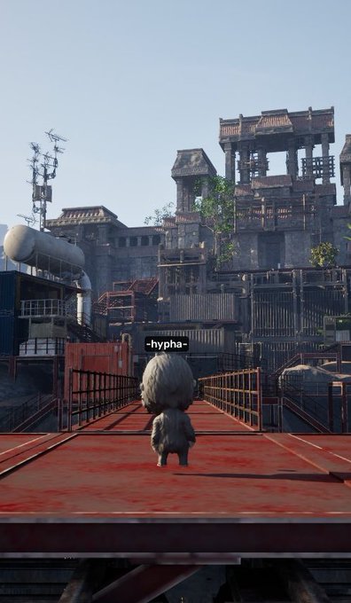 A small fluffy creature labeled '-hypha-' stands on a red industrial platform overlooking a vast post-apocalyptic industrial complex with dilapidated concrete buildings, pipes, and radio towers.