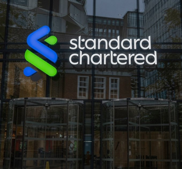 The image shows the Standard Chartered logo displayed on a glass building exterior, reflecting nearby city structures. The branding directly corresponds to the news that the $60 billion bank is expanding into crypto custody services for Singapore institutional clients.