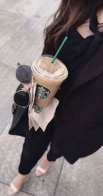 A woman in black carries a Starbucks iced coffee with a green straw alongside her sunglasses, pairing the brand's logo with her chill Friday "GM" post. The coffee serves as her morning fuel to match the upbeat, go-getter vibe of starting the day with good news.