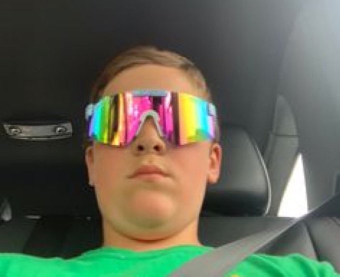 A young person wearing iridescent rainbow visor sunglasses sits in a car, channeling a flashy "Wall Street Bets" trader aesthetic. The caption leans into meme culture hype, playfully equating their flashy sunglasses look to the bravado of a legendary day trader celebrating gains ("tendies").