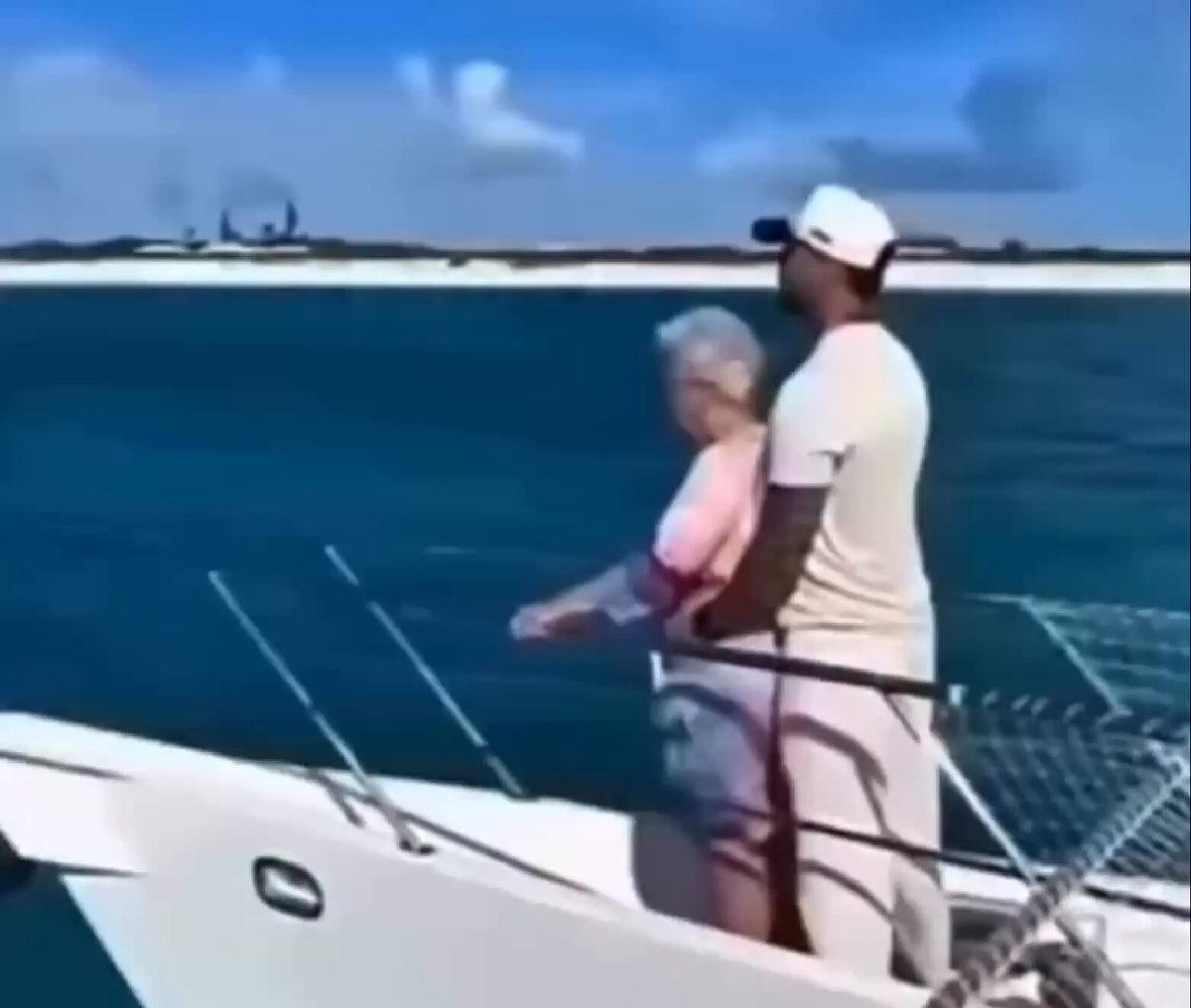 In the image, an older man and woman are standing side by side on a boat that appears white and blue. They seem to be enjoying their time together. The backdrop of this scene includes a beach with ocean water and several palm trees. A caption for the photo is provided: "Me with the $SPCX cafeteria lady after she becomes a millionaire from the IPO". This caption emphasizes that they are on a boat, likely having lunch or an outing near the shoreline during their leisure time.