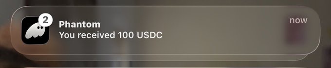 A Phantom wallet notification showing "Phantom - You received 100 USDC - now," supporting the post's claim of a $50 giveaway by demonstrating a recent USDC transfer in the creator's wallet as proof of funds.