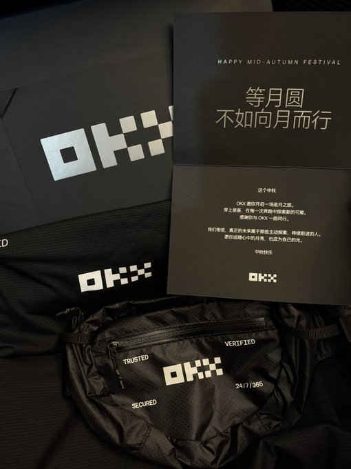 OKX cryptocurrency exchange branded merchandise and materials are displayed, including a black envelope, a card reading 'HAPPY MID-AUTUMN FESTIVAL 等月圆 不如向月而行', and a fanny pack labeled 'TRUSTED', 'VERIFIED', 'SECURED', and 'OKX'.