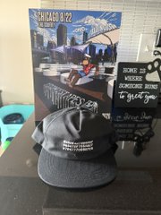 A gray baseball cap sits in front of a 'COLUMBUS 2022' welcome sign for the Short North Arts District, featuring a bicycle graphic and downtown skyline artwork.
