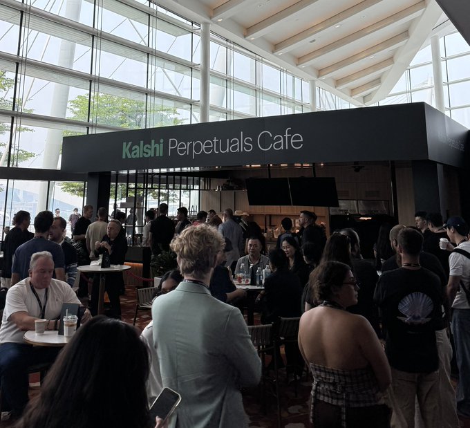 A crowded networking event inside the 'Kalshi Perpetuals Cafe' at a venue with high glass ceilings.