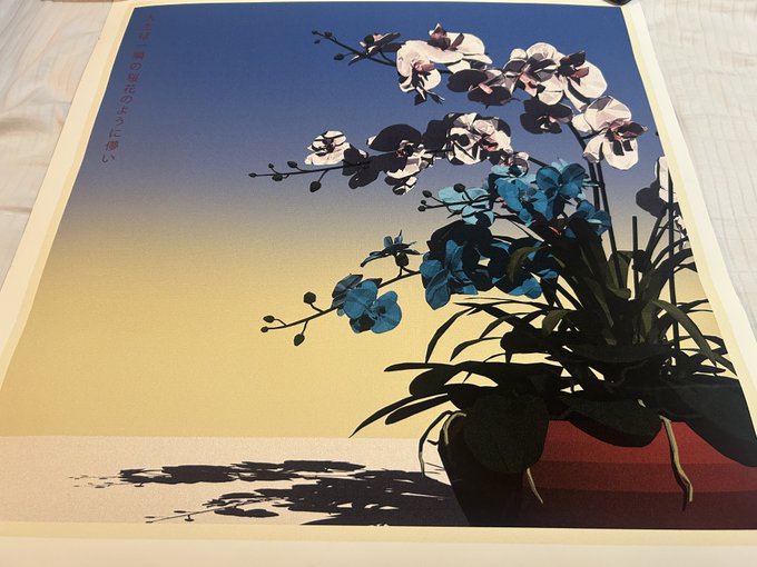 A framed art print depicting white and blue orchids in a vase against a gradient sky, with Japanese text running vertically along the left side.