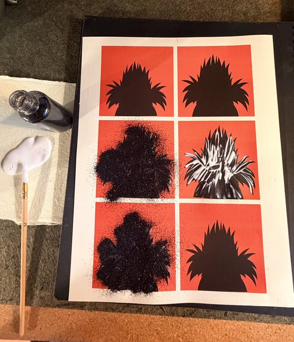 A spray paint art project in progress shows a grid of six red squares featuring black silhouettes of spiky-haired characters, with paint bottles and a brush resting beside it.