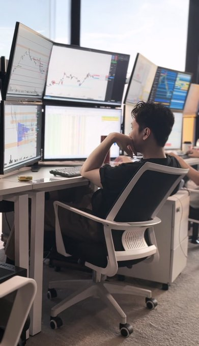 A young man sits at a multi-monitor trading setup displaying various charts and graphs, deeply focused while resting his chin on his hand. The scene visually reinforces the post's narrative of a savvy quant trader leveraging algorithmic bots and market inefficiencies to generate substantial crypto trading profits.