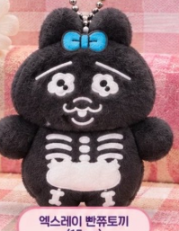 A small, black plush keychain figure resembling a bear or xpe with a blue bow, a white skeleton design, and Korean text '엑스레이 반죽토끼' (X-ray Bunny dough) on a pink label.