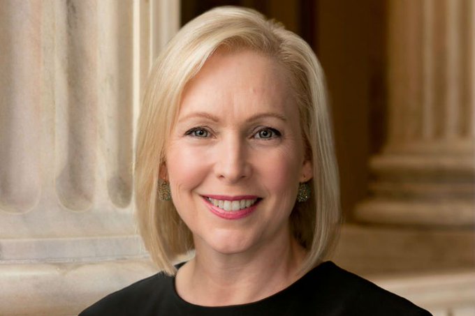A professional headshot of Senator Kirsten Gillibrand, a blonde woman wearing a black top and gold earrings, smiling against a backdrop of classical columns—aligning with the post about her pivotal role in advancing the CLARITY Act despite pushback from fellow Democrats.