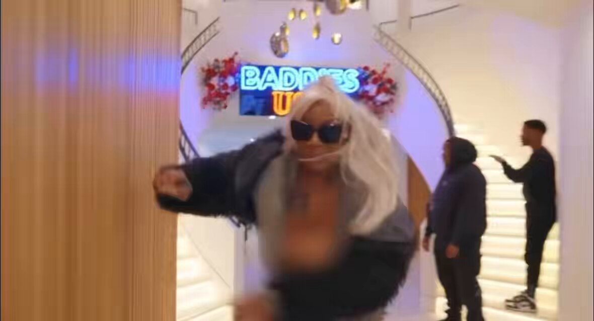 The image shows a woman wearing sunglasses, with her arm outstretched towards the camera. She appears to be dancing or engaging in some sort of performance. In the background, there are two men present - one standing near a staircase and another person who is not visible in the frame. The text "GETHER" can also be seen in the image.