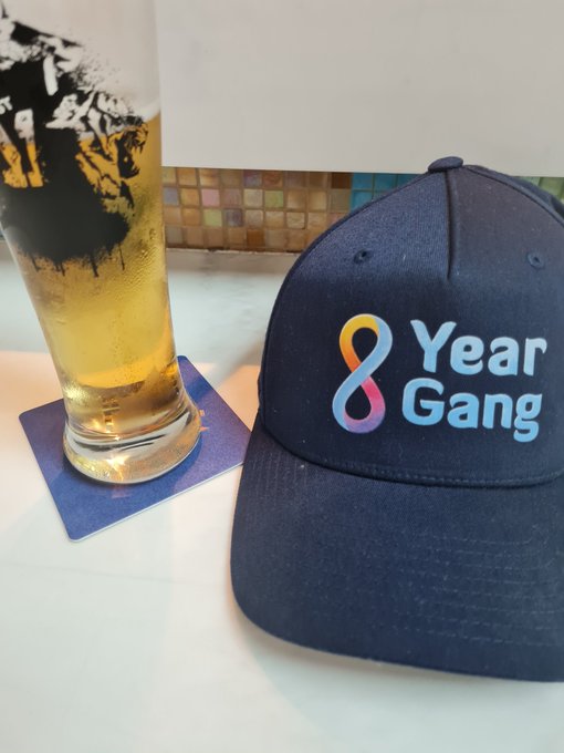 The image features a blue baseball cap with the words "Year Gang" written on it, placed next to a glass of beer. The caption reads "Focus on what is in the image and how it relates to the post".
