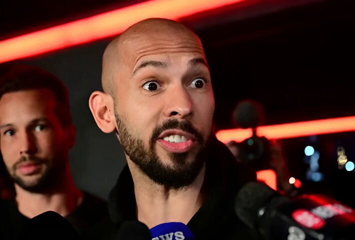 The image features a man wearing a black shirt with a microphone in front of him, suggesting that he is speaking or recording something. He appears to be dressed in athletic attire, possibly indicating his involvement in sports. The background has a red glow, which might represent the setting for an event or an interview taking place on this particular platform. The post is titled "ÚLTIMA HORA: EL LONG DEBITCOIN Á CERCA DE LA LIQUIDACIÓN TATE, QUE HA SIDO LIQUIDADO 107 VECES (NUEVO RÉCORD), ACABA de ABRIR UN LONG DE BITCOIN 40X EN HYPERLIQUID. LA POSICIÓN VALE 57.36 BTC, O APROXIMADAMENTE $3.76 MILLONES". The main focus of the image is on this man and his interaction with the camera or microphone in front of him.
