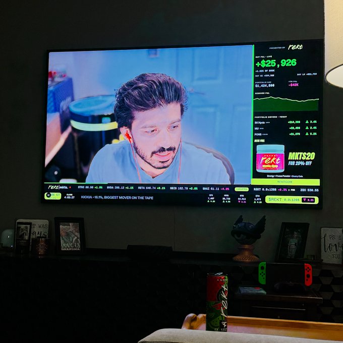 A television screen showing a stock market broadcast on Robinhood featuring a presenter wearing red earbuds, with a portfolio showing '+$25,926' and an MKTS20 promo.