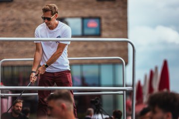 A man in a white shirt and maroon shorts wearing sunglasses stands on a balcony overlooking a crowd at what appears to be an outdoor Solana Summit event, with the brick building and cloudy sky in the background. The image relates to the event's activity poll, possibly depicting one of the fun activities like golfing or hanging game that attendees enjoyed during Solana Summit Germany.