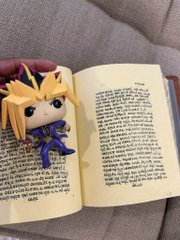 A small handmade plush figure of a blonde anime-style character with a purple outfit sits on an open book with blurred text, while a tiny "$PUMP coded" handcrafted doll character mirrors the post's theme of meme-driven token hype.
