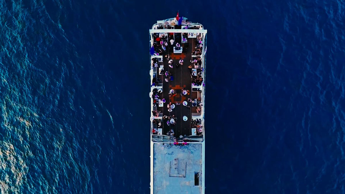 The image shows a large boat sailing across the ocean with several people onboard enjoying their time together. The boat appears to be a cruise ship, as evidenced by its size and the number of passengers present. The scene captures a moment where everyone on board is having fun and making memories during their journey.