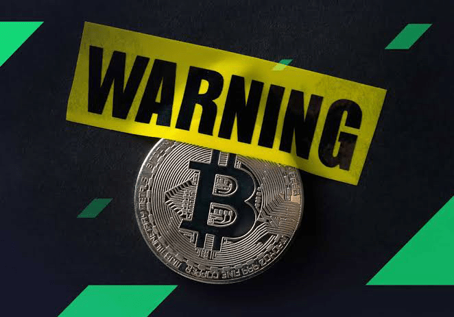 A silver physical Bitcoin coin displayed on a dark surface with green geometric accents, overlaid with yellow 'WARNING' tape.