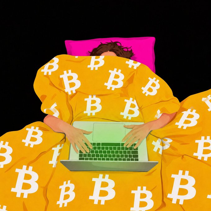 An illustration depicts a person lying in bed under a yellow Bitcoin-patterned blanket using a laptop, with only their hands and laptop visible on a pink pillow.