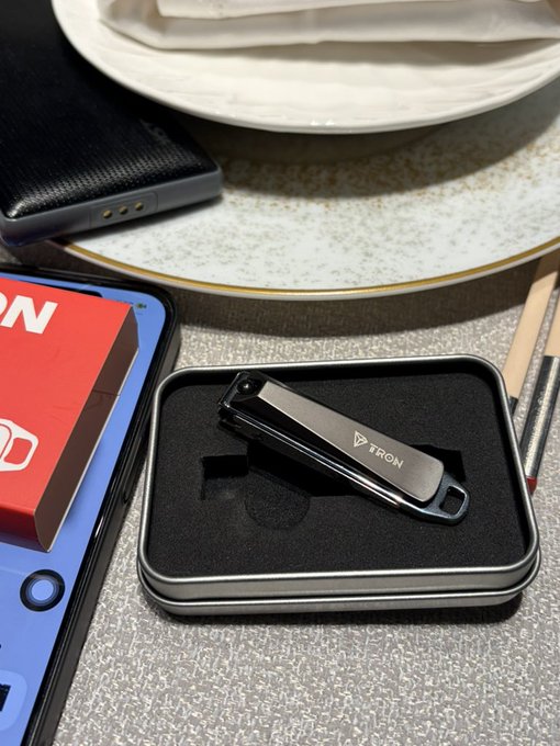 A photo of a black titanium key organizer branded 'TIRION' displayed in its black metal tin case, sitting on a table next to a phone and a red box.