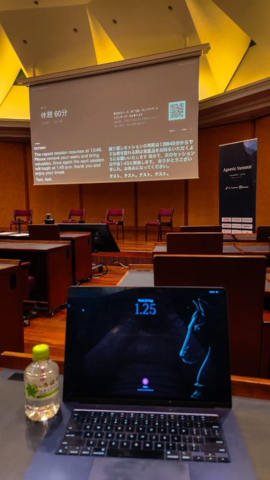 A laptop on a desk in a lecture hall displays '1.25' with a horse image, while a presentation screen behind shows Japanese text and a 60-minute timer.