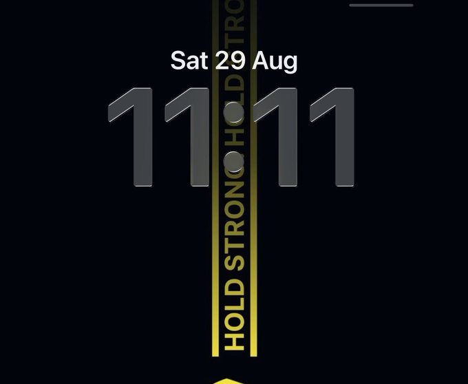 A minimalist smartphone wallpaper displaying the time '11:11', the date 'Sat 29 Aug', and the vertical text 'HOLD STRONG HOLD STRONG' in yellow.