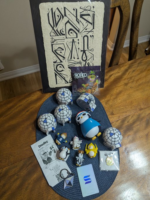 An arrangement of Solana ecosystem merchandise and collectibles on a blue placemat, including Doodles plush toys, a Solana keychain, a trading card, and a decorative pillow.