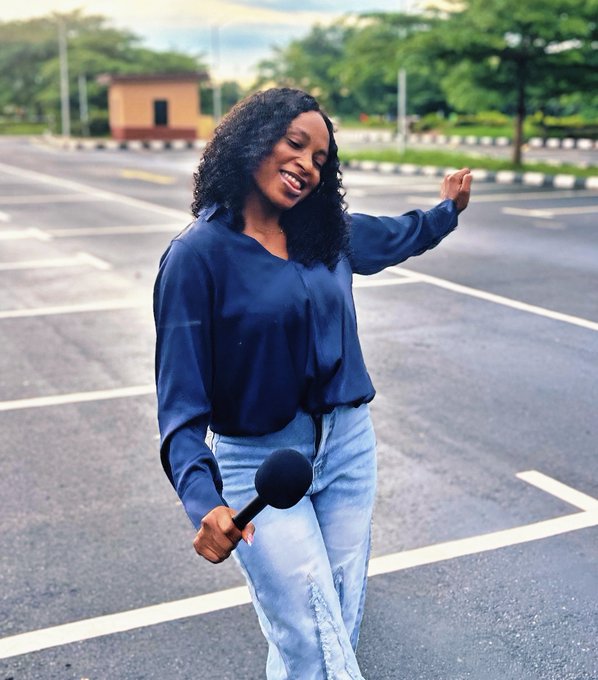 A woman with curly hair dances joyfully in an empty parking lot, holding a microphone in a navy blue blouse and light jeans, perfectly capturing the playful "AI on the Street" vibe as she celebrates the upcoming AI x Web3 video drop.