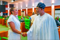 Two medical professionals, a woman in scrubs and a man in surgical attire, shaking hands in what appears to be a conference hall setting.