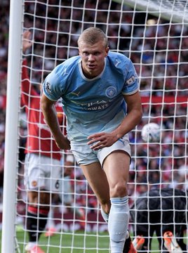Erling Haaland, wearing the light blue Manchester City jersey with the Etihad Airways sponsor, appears focused near the goal net during the match. The image connects to the post by visually capturing the star striker whose performance powered Manchester City's victory over Manchester United, further diminishing United's fading Premier League title hopes.