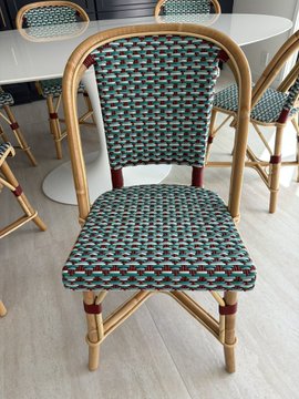 A green and white woven rattan bistro-style chair with red accents, displayed in what appears to be a furniture showroom.