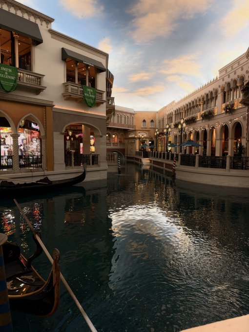 A Venetian-style indoor canal at The Venetian resort with gondolas, featuring Smith & Wollensky restaurant banners and reflections in the water beneath a sunset sky.