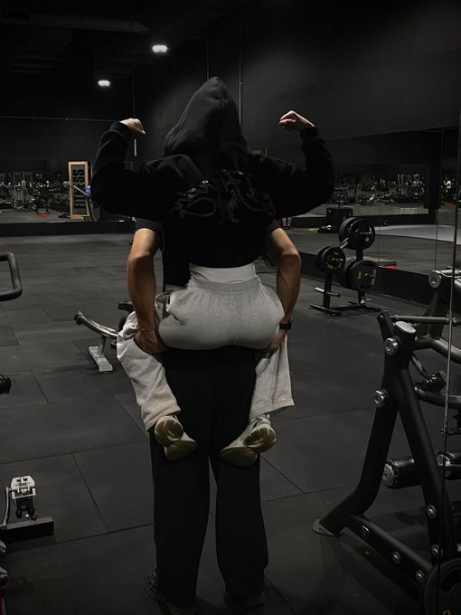 A photo taken in a gym showing a person doing a piggyback ride on another person's back while flexing their arms.