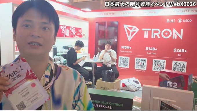 A man holds a "WebX 2026" badge in front of a large TRON booth at Japan's largest crypto event, with promotional signage displaying "TRON," "USDD," "390M+ Total Accounts," "$14B+ Total Txns," and "$26B+ TVL." The booth prominently showcases TRX and the TRC20 network, aligning with the post's praise of TRON's strong presence and recent success.