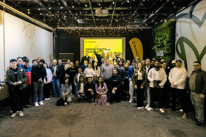 The image shows a large group of attendees posing together at the "Group Photo" moment of the Binance 9th Anniversary event in ANZ, with visible branding including "BINANCE," "GROUP PHOTO," and the "Binance" flag, capturing the community spirit that the post highlights as the event's most memorable aspect.