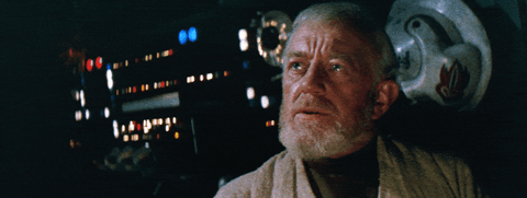 A close-up shot of an older bearded man (Obi-Wan Kenobi from Star Wars) inside a dimly lit spacecraft cockpit with illuminated control panels.