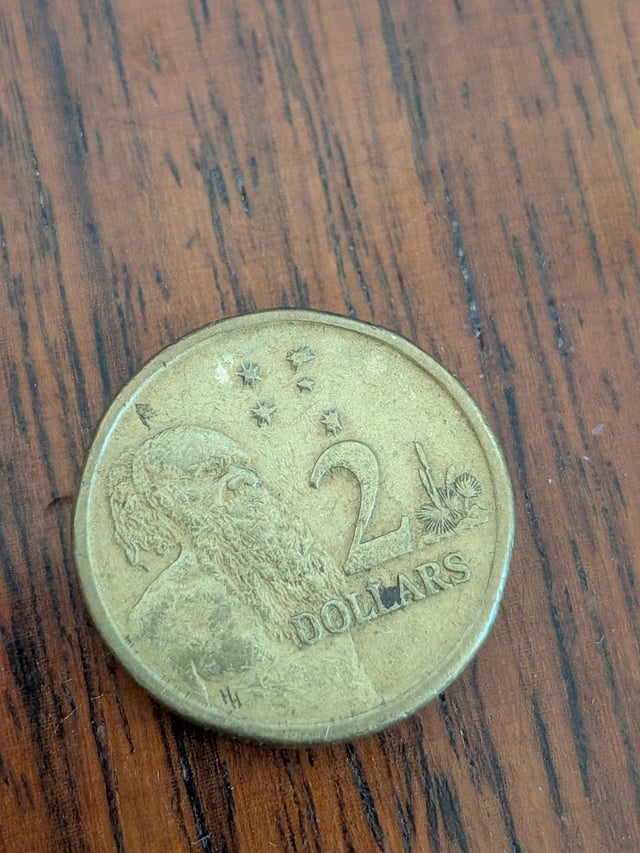 An Australian 2 dollar coin featuring a platypus design, resting on a wooden surface.