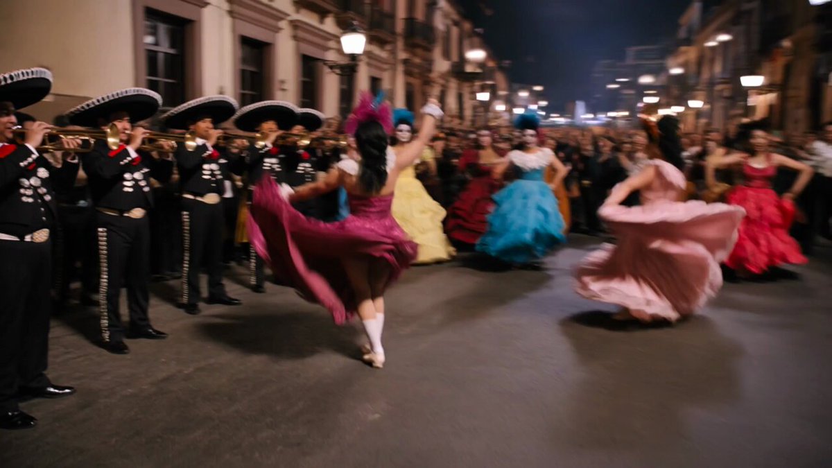The image shows a group of people dancing at night with colorful dresses and sombreros. The dancers are wearing traditional Mexican costumes and hats, which adds to the festive atmosphere. The photo captures the essence of a lively celebration or parade taking place in Mexico City's streets.